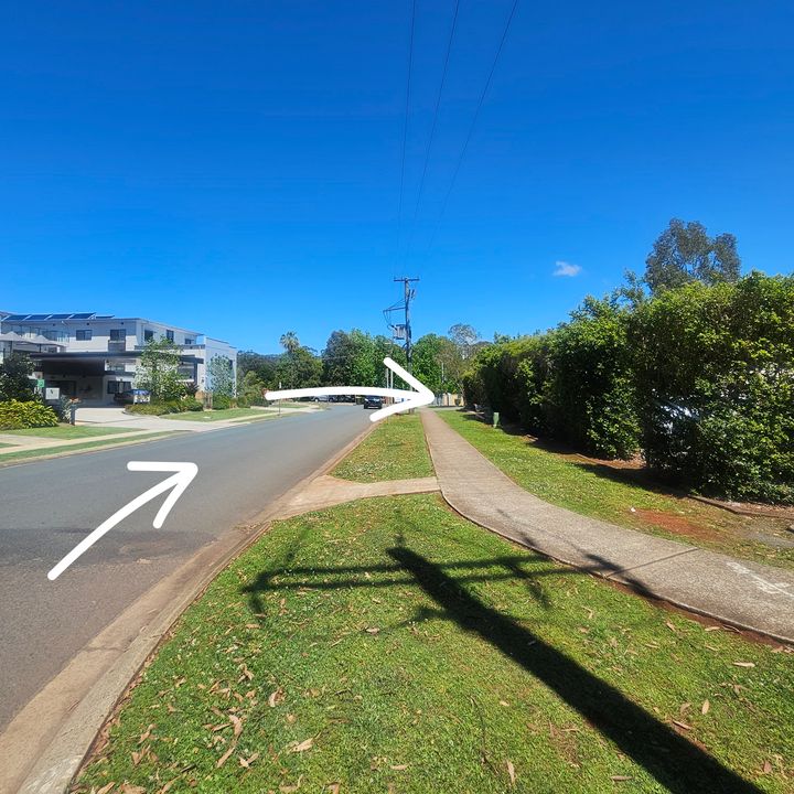 Street with a tall hedge on the right, with white arrows showing where to turn right
